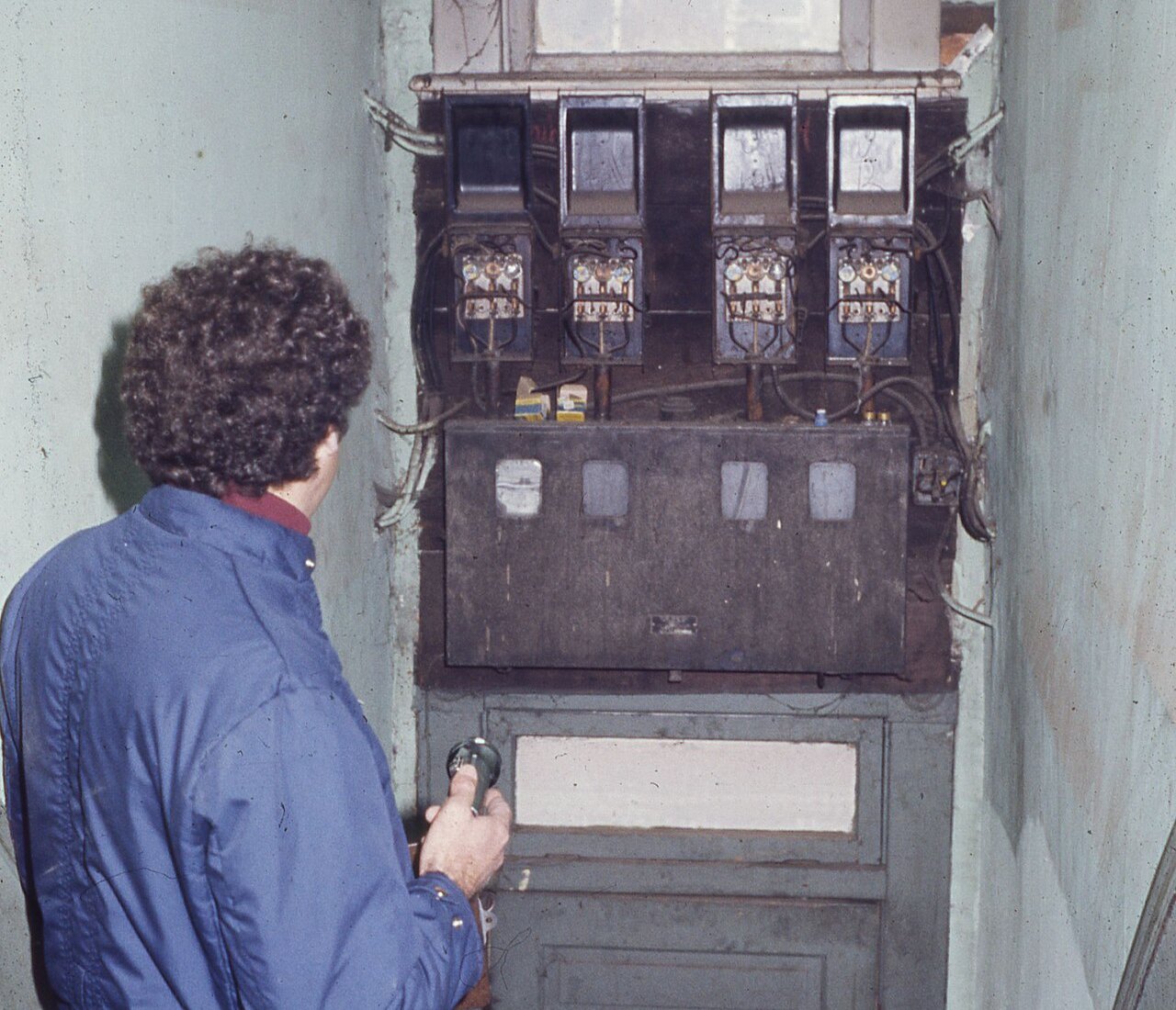 A home inspector with a flashlight examining old electrical wiring in the stairway of a house